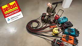 Werkstattsauger-Test Ein Mann sitzt auf dem Boden, umgeben von acht Werkstattsaugern mit langen, ausgebreiteten Schläuchen.