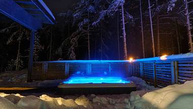 Ein beleuchtete Whirlpool lädt zum Entspannen in der wunderschönen Winterlandschaft unter den Sternen ein. - Foto: iStock / :Finmiki Images