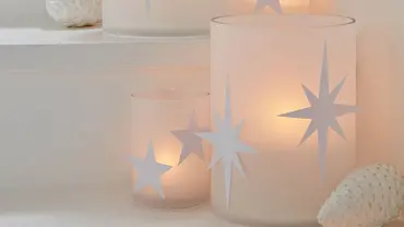 Filigrane Weihnachts-Windlichter aus weißem Transparentpapier vor Tannenzapfen-Deko - Foto: Hersteller / tesa SE